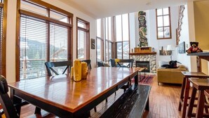 A spacious living area with a large wooden table, comfortable seating, and a stone fireplace. - Woodhaven #11 by Bear Country (Sun Peaks)