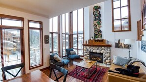 A spacious living room with large windows, a stone fireplace, and a cozy seating area. - Woodhaven #11 by Bear Country (Sun Peaks)