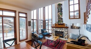 A spacious living room with large windows, a stone fireplace, and a cozy seating area. - Woodhaven #11 by Bear Country (Sun Peaks)