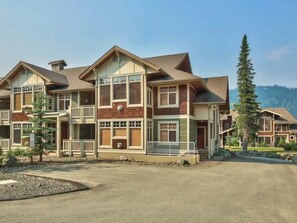 A multi-story hotel with a central courtyard, balconies, and a mountain backdrop. - Settlers Crossing #61 by Bear Country (Sun Peaks)