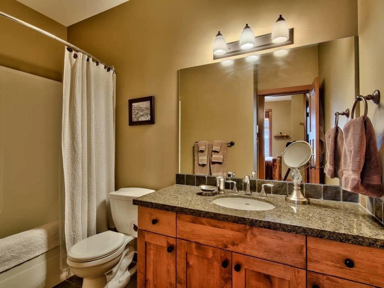 A bathroom with a wooden vanity, a sink, a mirror, and a shower curtain.