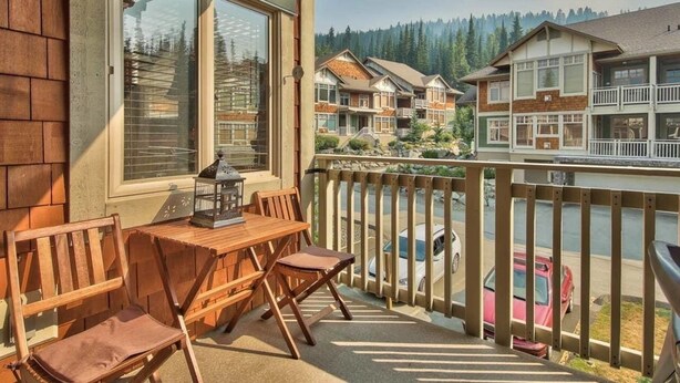 Eine Holzterrasse mit Tisch und Stühlen, mit Blick auf einen See und eine Reihe von Häusern.