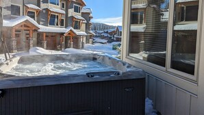 A hot tub in a snowy outdoor setting with a view of a mountain and a lodge in the background. - Echo Landing #12 by Bear Country (Sun Peaks)