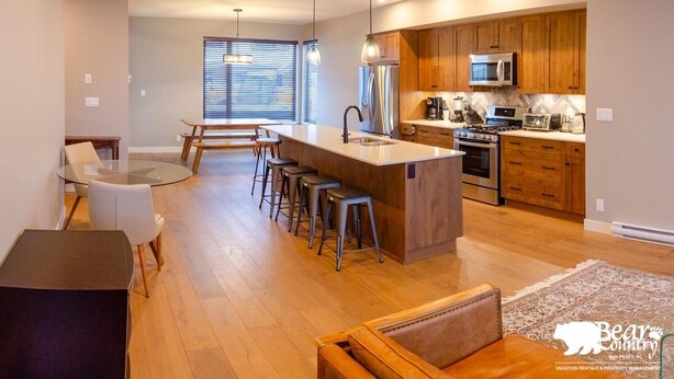 A modern kitchen with wooden cabinets, stainless steel appliances, and a central island with bar stools. - Echo Landing #12 by Bear Country (Sun Peaks)