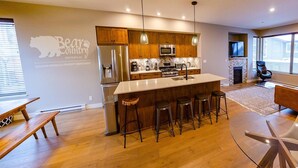A modern kitchen with wooden cabinets, stainless steel appliances, and a central island with stools. - Echo Landing #12 by Bear Country (Sun Peaks)
