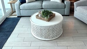 A modern living room with a grey sofa, a round coffee table, and a patterned armchair. There are framed artworks on the wall and a lamp on a side table. - Beautiful Beachfront 2 Bed/2 Bath Condo - Walk to Hangout and Great Rates (Gulf Shores)