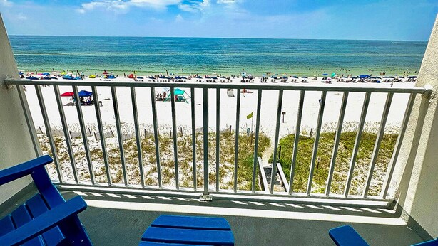 A balcony with a view of a beach and ocean. There are two blue chairs and a small table. - Beautiful Beachfront 2 Bed/2 Bath Condo - Walk to Hangout and Great Rates (Gulf Shores)
