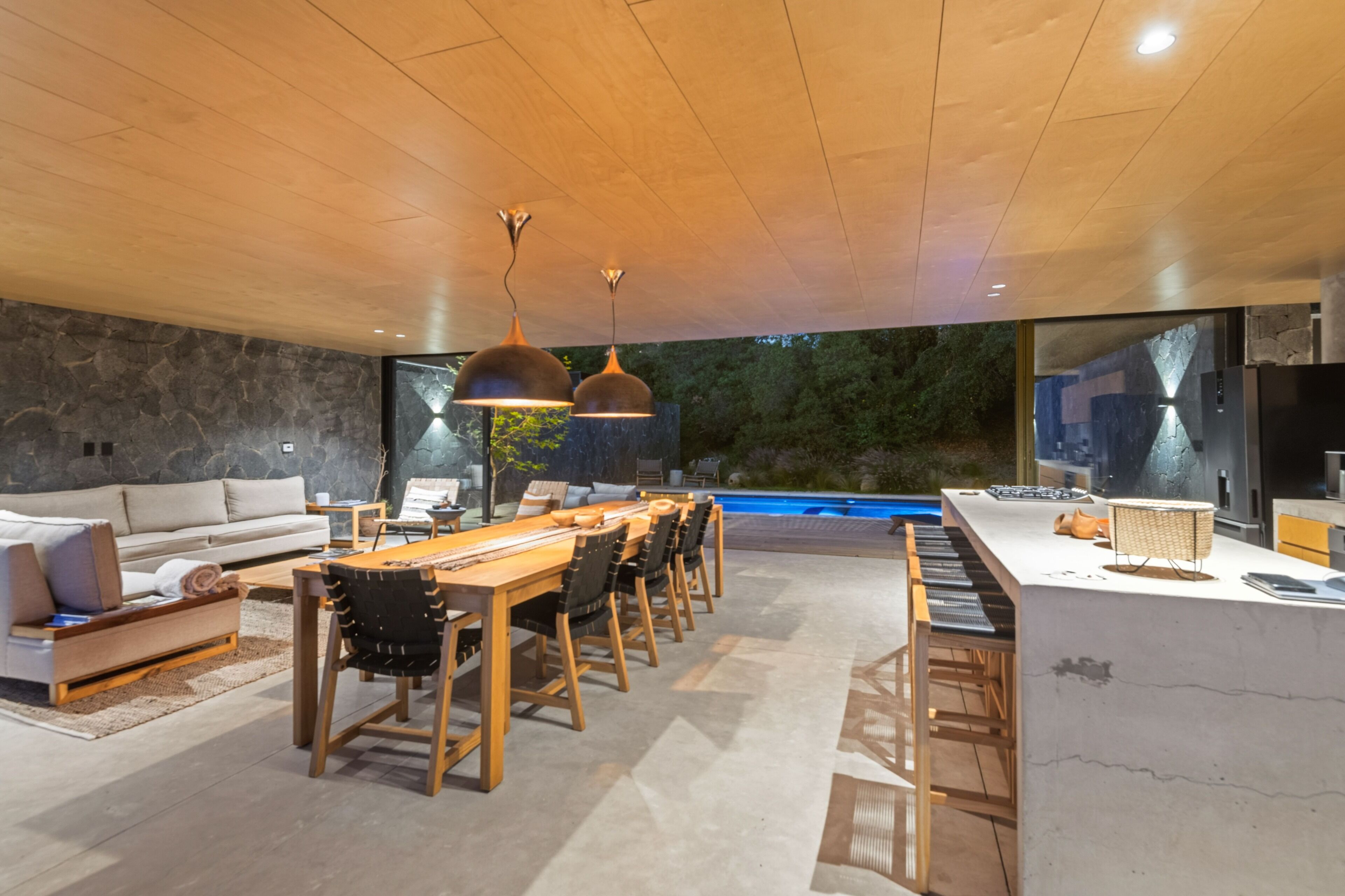 Una cocina moderna con una isla grande, una zona de comedor con una mesa larga y sillas, y vista a una piscina.