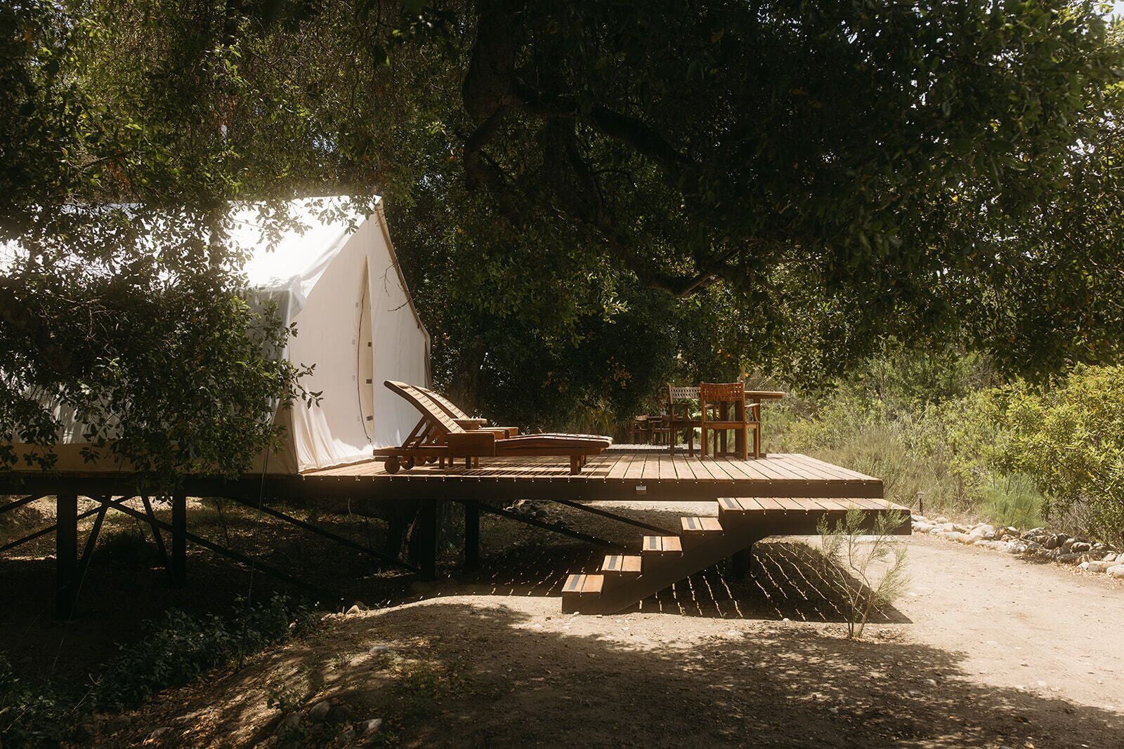 Un patio di legno con poltrone da relax e un tavolo, immerso nel verde.