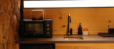 A compact kitchen with a microwave, sink, and dishwasher, featuring wooden cabinetry and a stone accent wall.