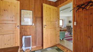 Un intérieur en bois avec un radiateur, un tableau encadré et une vue sur une pièce où se trouvent une table et une chaise.