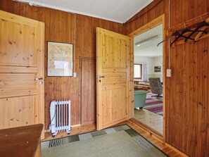 Interior de madera con un radiador, un cuadro enmarcado y vista a un cuarto con una mesa y una silla.
