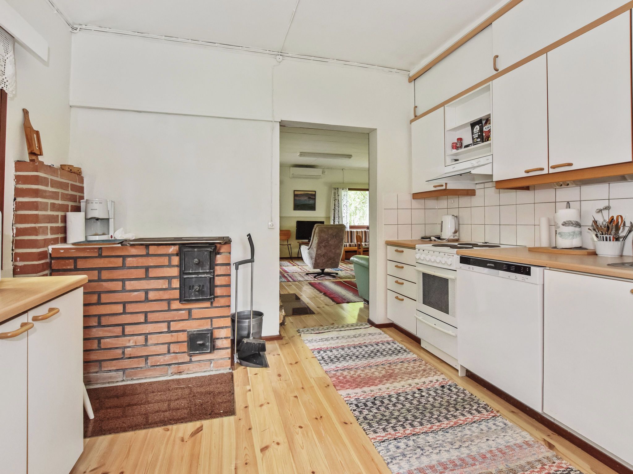 Una cocina con pared de ladrillo, armarios blancos, estufa y lavavajillas.
