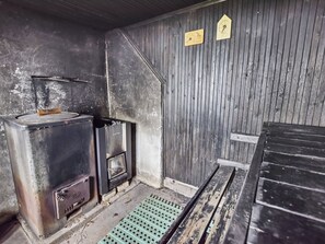 A room with a metal stove, a wooden bench, and a wooden wall with two wooden signs.