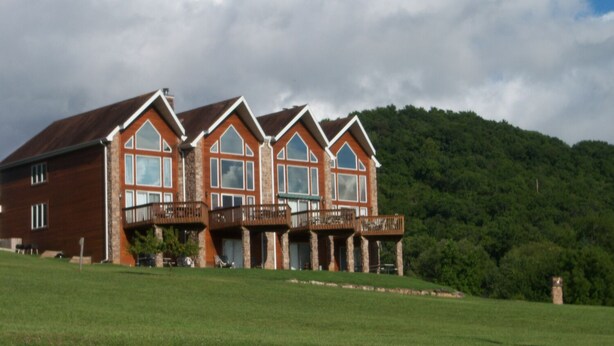 A large, multi-story building with a prominent balcony area, set against a backdrop of lush green hills and a partly cloudy sky. - Table Rock Lake, Steps to Marina (Holiday Island)