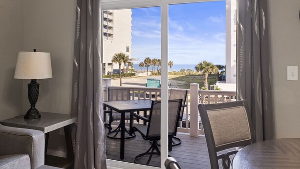 Een balkon met een tafel en stoelen, een lamp en uitzicht op het strand en palmbomen.