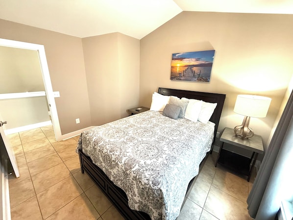 A bedroom with a bed, nightstands, a lamp, a painting, and a door.