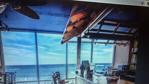 A modern interior with large windows overlooking the ocean, a wooden ceiling, and a bar area.