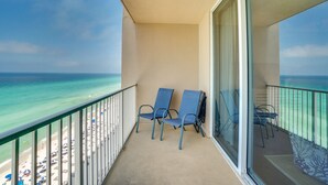 A balcony with two chairs overlooking a beach and the ocean.