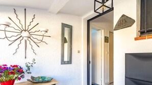 Un couloir agrémenté d’un luminaire moderne, d’un miroir, d’une petite table sur laquelle se trouvent un vase et des fleurs, et d’une porte donnant sur une autre pièce.