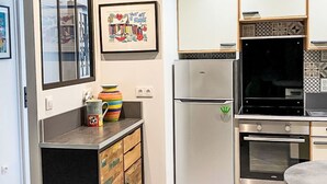 Une cuisine moderne équipée d’un four encastré, d’un réfrigérateur et d’un four à micro-ondes. On y trouve un meuble en bois sur lequel est posée une tasse colorée.