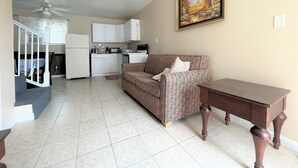 A living room with a patterned sofa, a wooden table, and a kitchen in the background.