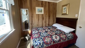 A bedroom with a wooden paneled wall, a bed with a patterned quilt, a mirror, and a framed picture on the wall.
