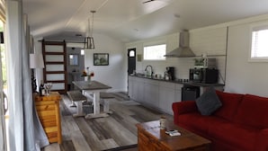 A spacious living area with a red sofa, wooden coffee table, and a dining table with benches. A kitchen with white cabinets and a microwave is visible in the background.