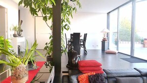 Un salon moderne avec un canapé en cuir noir, des coussins rouges et une grande fenêtre donnant sur l’extérieur.