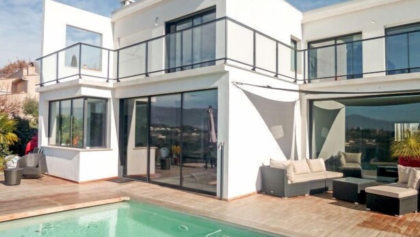 Une maison moderne à deux étages, dotée d’une piscine, d’un espace salon extérieur et de grandes fenêtres.
