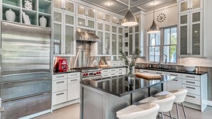 Una cocina moderna con electrodomésticos de acero inoxidable, una isla central con taburetes de bar y armarios blancos con puertas de vidrio esmerilado.