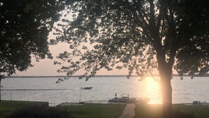 Blick auf das Wasser mit einem Weg zum Steg, Booten auf dem Wasser und einem Sonnenuntergang im Hintergrund.