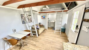 Un espacio habitable compacto con cama elevada, zona de comedor con mesa y sillas, kitchenette y baño.