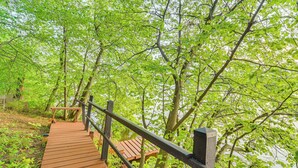 A wooden bridge leading to a bench and a gazebo in a lush green forest. - Lakefront Family Retreat w/ Private Dock! (Rice Lake)