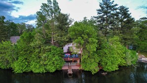A house surrounded by dense trees on a lake, with a dock leading to the water. - Lakefront Family Retreat w/ Private Dock! (Rice Lake)