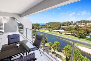 Ein Balkon mit Glastisch und Stühlen, mit Blick auf einen Golfplatz und einen Fluss.
