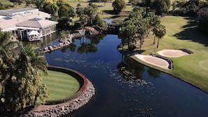 Un campo de golf con un estanque, palmeras y un edificio con techo.