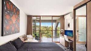 Una habitación de hotel moderna con una cama grande, un escritorio con computadora y un balcón con vistas.