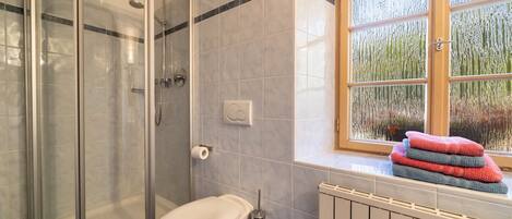 Et badeværelse med bruseniche, toilet, et vindue med udsigt og en radiator.
