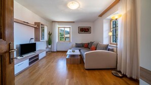 Una sala de estar con sofá, mesa de centro, televisor y una ventana con cortinas.