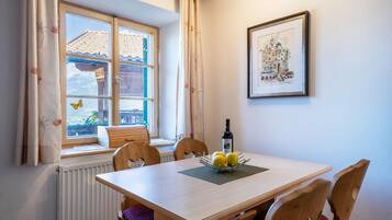 A dining area with a table, chairs, a window with curtains, a radiator, and a framed picture on the wall.