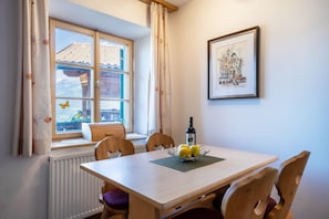 A dining area with a table, chairs, a window with curtains, a radiator, and a framed picture on the wall.