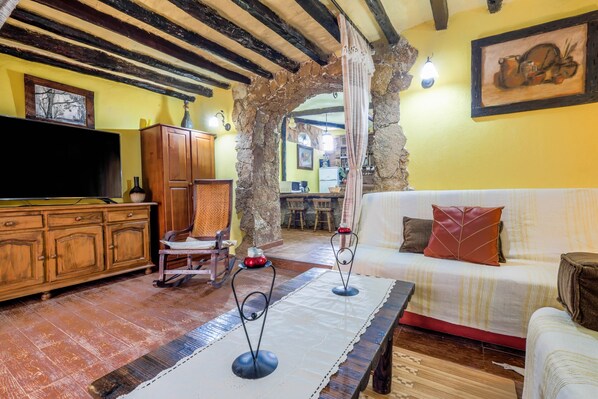 A rustic living room with exposed beams, a wooden cabinet, a flat-screen TV, a sofa, and a table with candle holders.