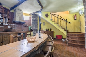 A rustic kitchen with a stone wall, wooden bar, and a staircase leading to a second floor.