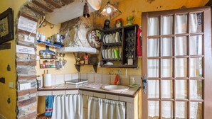 A kitchen with a stone wall, a sink, a window with curtains, and various kitchen items on shelves.