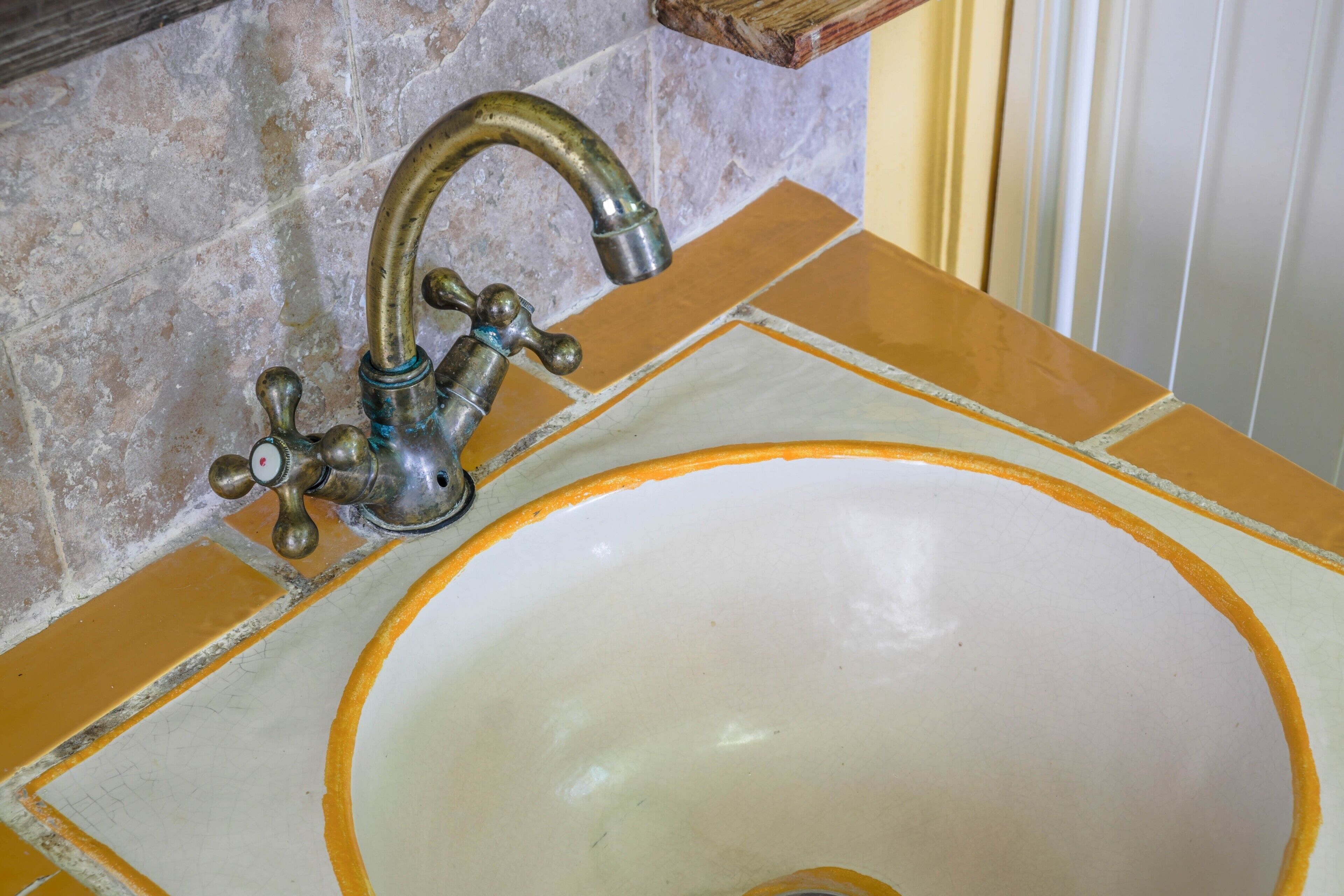 A bathroom sink with a vintage faucet and a white basin with an orange rim.
