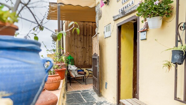 A narrow alleyway with a wooden bench, potted plants, and a door leading to a building with a sign.