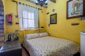 Quarto com cama, um banco, extintor de incêndio, janela com cortinas e um quadro na parede.