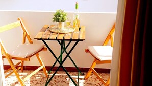 Un petit balcon avec une table en bois, deux chaises, un pot de fleurs et une bouteille de vin.