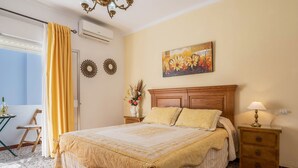 Une chambre à coucher comprenant un lit, une table de chevet, une lampe, une fenêtre avec des rideaux, un miroir fixé au mur et un tableau.